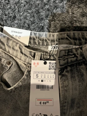 Grå raka jeans från ZARA - Säljer ett par grå raka jeans från ZARA i storlek S/26. Jeansen har en straight fit, klassisk femficksdesign och råa kanter vid bensluten för en trendig look. Perfekta till sneakers eller boots och passar till många olika stilar.