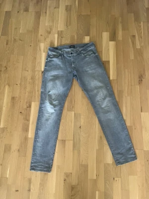 Grå slim fit jeans från Jack & Jones - Snygga grå slim fit jeans från Jack & Jones med klassisk femficksdesign och dragkedjegylf. Jeansen har en tvättad look och raka ben som sitter tajt hela vägen ner. Perfekta för en avslappnad och trendig stil.