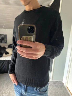 Uniqlo tröja - En enkel svart stickad tröja med rund halsringning och ribbade muddar vid ärmslut och nederkant. Perfekt till jeans eller över en skjorta för en clean look. Passar dig som gillar minimalistisk stil.
