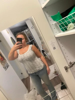 Vit spetslinne med blommönster - Säljer ett vitt linne med spetsdetaljer och blommönster. Linnet har breda axelband och en feminin, figurnära passform. Perfekt att styla med jeans eller kjol för en trendig look. Materialet känns lätt och luftigt.