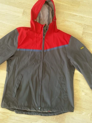 Barbour vindjacka marinblå/vinröd stl M - Snygg vindjacka från Barbour i storlek M. Jackan har vinröd ovandel, marinblå nederdel och en blå rand över bröstet. Utrustad med huva, dragkedja och två sidofickor. Meshfoder på insidan för extra komfort. Perfekt för blåsiga dagar. Mycket fint skick. Har dock spruckit lite i innefodret (se bild) men går att laga om man vill. 