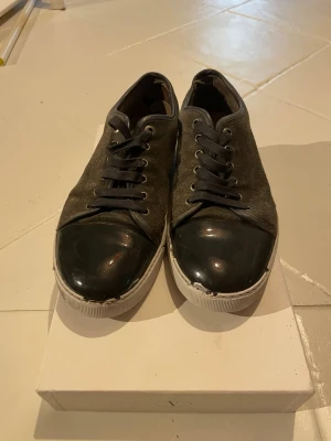 Lanvin sneakers - Säljer ett par riktigt feta Lanvin sneakers i storlek 41. Klassisk modell med mörk mocka, svarta detaljer och vita sulor.  Skorna är använda och har tecken på användning, se bilder för skick och detaljer. Säljes i befintligt skick.  📏 Storlek: 41 📦 Skick: Använda – se bilder 🚚 Skickas snabbt och packas ordentligt.  Hör gärna av dig vid frågor!