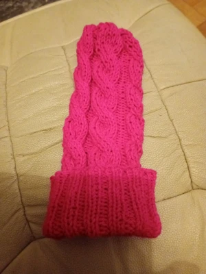 Rosa kabelstickad mössa barn mörkrosa - Säljer en snygg rosa kabelstickad mössa med uppvikt kant. Mössan är gjord i ett mjukt garn och har ett klassiskt flätmönster som ger en trendig look. Perfekt för att hålla värmen under kyliga dagar och passar till de flesta outfits.