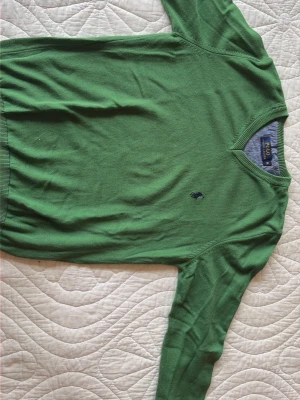 Grön stickad tröja Polo Ralph Lauren - Grön stickad tröja från Polo Ralph Lauren med v-ringning och klassisk broderad logga på bröstet. Tröjan har långa ärmar och ribbade muddar vid hals, ärmslut och nederkant.  