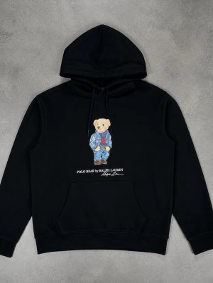 Polo Bear Ralph Lauren - Säljer en mörkblå hoodie från Ralph Lauren med den ikoniska Polo Bear-trycket framtill. Hoodien har huva med dragsko och en stor magficka. Materialet är mjukt och skönt, perfekt för en chill och avslappnad stil.