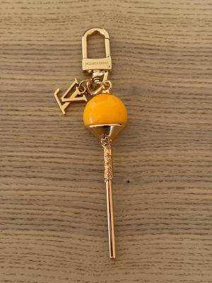  Vuitton nyckelring klubba gul - Unik nyckelring från  Vuitton formad som en klubba i gul och guldfärgad metall. Har LV-logga som charm och karbinhake med ingraverad logotyp. Perfekt accessoar för att piffa upp väskan eller nyckelknippan.