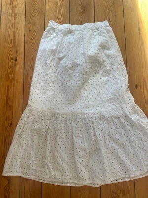 Vit kjol med broderade detaljer - Säljer en vit midi-kjol med hålmönster, resår i midjan och volang nedtill. Barnstorlek 170 men passar som S/Xs. Ett litet hål som syns på sista bilden