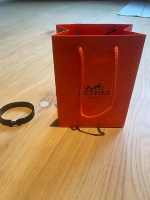 Svart armband från H med påse  - Snyggt svart armband från H i metall med klassisk H-detalj framtill. Armbandet har en stilren och modern design som passar perfekt till din outfit. Levereras med original orange H-påse. Postar oftast samma dag, pris kan diskuteras.