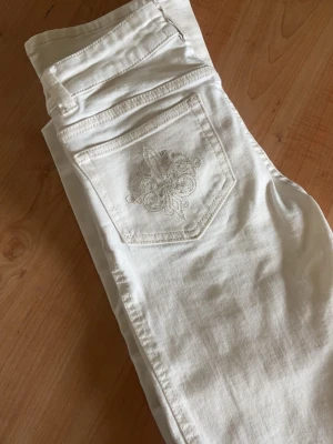 Vita jeans med broderad bakficka - Snygga vita jeans med rak passform och broderad detalj på bakfickan. Jeansen har klassisk femficksdesign och är tillverkade i ett mjukt denimtyg som känns bekvämt hela dagen.