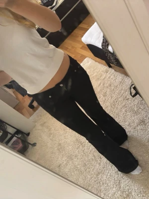 Vit kortärmad  tröja - Säljer ett par svarta bootcut jeans med låg midja och silverfärgade knappar. Jeansen har klassisk femficksdesign och är gjorda i ett stretchigt material som sitter snyggt och bekvämt. Perfekta för dig som gillar en trendig och avslappnad stil.
