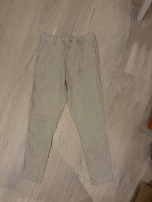 Beiga linnebyxor med dragsko - Snygga beiga linnebyxor med avslappnad passform och dragsko i midjan. Byxorna har sidofickor fram och två passpoalfickor bak. Perfekta för en chill och stilren look under varmare dagar. Tillverkade i luftigt linnematerial. Linneblandning. Strl 36/passar S Aldrig använda 😀