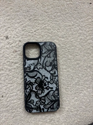 Svart mobilskal med spetsmönster - Snyggt svart mobilskal med detaljerat spetsmönster i vitt och svart. Skalets baksida har ett blommigt och elegant designat mönster som ger mobilen en unik look. Tillverkat i tåligt plastmaterial och passar modeller med större kameralins.