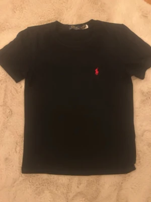 Svart t-shirt från Polo Ralph Lauren - Klassisk svart t-shirt från Polo Ralph Lauren med korta ärmar och rund hals. På bröstet finns den ikoniska rosa logotypen broderad. Tillverkad i mjuk bomull för en skön och avslappnad stil. Den sitter lite mindre så den är mer som en XS, andvänd fåtal gånger under förra sommaren men inget som har tagit stryk förutom qr koden. Jag har även en likadan fast i vit som jag kan fixa bra pris med båda.