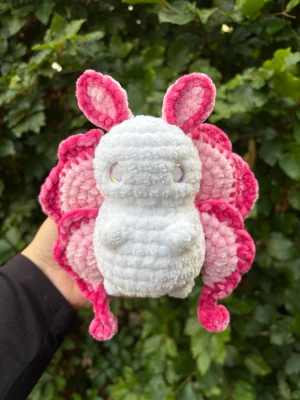 Virkad rosa fjärilsfe🩷 - Supergullig virkad fjärilsfigur i mjukt garn. Kroppen är vit och vingarna är rosa med olika nyanser. Den har stora öron och små armar, perfekt som dekoration eller present till någon som gillar söta saker. Rekommenderar inte till småbarn eftersom ögonen utgör en kvävningsrisk!