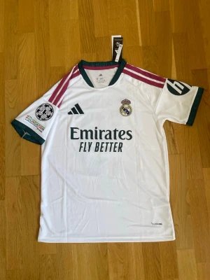 Real Madrid hemmatröja 2026/27 - Real Madrid hemmatröja från säsongen 2026/27 med Champions League patch. Storlek M. Helt ny med prislapp och aldrig använd. Perfekt för samlare, fotbollsfans eller vardagsbruk.