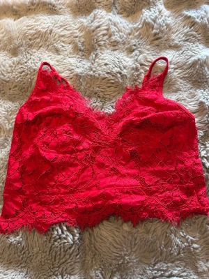 Röd spetsbralette med blommönster - Säljer en snygg röd bralette i spets med blommigt mönster och tunna axelband. Braletten har en mjuk och stretchig känsla, samt fina spetsdetaljer längs kanterna. Perfekt för dig som gillar feminina och trendiga underkläder.