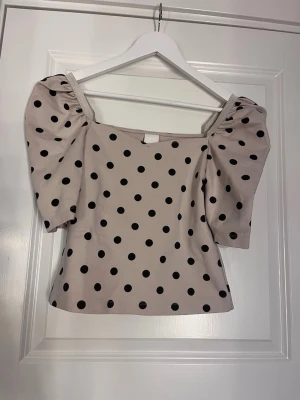 Prickig topp med puffärm - Supersöt topp med puffiga ärmar och svart prickigt mönster på ljus botten. Fyrkantig ringning och figurnära passform, passar perfekt för festligare tillfällen!