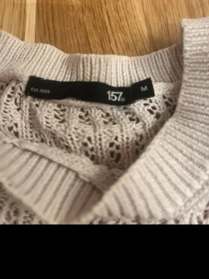 Vit stickad tröja från 157 - Snygg vit stickad tröja från 157 med korta ärmar och rund hals. Tröjan har ett genombrutet mönster och ribbade muddar vid hals, ärmslut och nederkant. Perfekt för lager på lager och ger en fräsch look till din outfit.