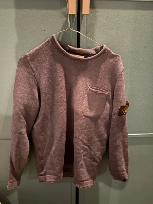 Mörk blå stickad tröja från Stone Island - Snygg mörk blå stickad tröja från Stone Island med rund halsringning och liten bröstficka. Tröjan har lång ärm och klassisk logotyp på ärmen. Perfekt för dig som gillar streetwear och vill ha något unikt i garderoben.