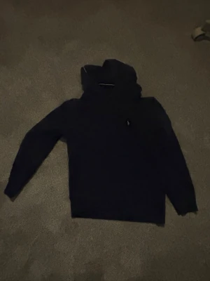 Mörkblå hoodie från Polo Ralph Lauren - Snygg mörkblå hoodie från Polo Ralph Lauren med klassisk huva och känguruficka. Liten broderad logga på bröstet. Tillverkad i mjukt material som känns skönt mot huden. Perfekt för en avslappnad och stilren look. Pris kan sänkas lite