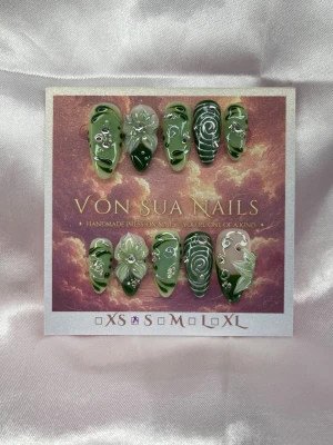 Viridi (S);Medium Almond - Handgjorda press-on naglar i olika gröna nyanser med swirl-mönster, blommor och silverdetaljer. Naglarna har en medium lång  almondform och dekoreras med handgjorda 3D-blommor och små kristaller för extra effekt. Perfekt för dig som vill ha unika och kreativa naglar.S: 15 mm, 11,5 mm, 12 mm, 11 mm, 9 mm 