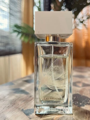 Elizabeth Arden White Tea Eau Fraiche EdT,50ml - Elegant parfymflaska i genomskinligt glas med vit fyrkantig kork och guldigt spraymunstycke. Flaskan har en stilren design med texten 'Eau Fraiche' på framsidan och ett subtilt mönster på insidan. Perfekt för dig som gillar fräscha dofter.