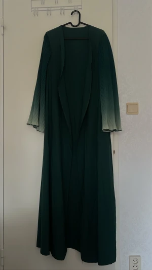 Mörkgrön lång abaya - Snygg mörkgrön abaya/lång kläning. Den har öppen front och ett elegant fall. Är ungefär 142-143 cm lång, passar för dig som vill sticka ut med en unik och trendig look🥰 köptes från shein och är endast endast använd en gång! Säljer den nu då den inte var min typ riktigt(: