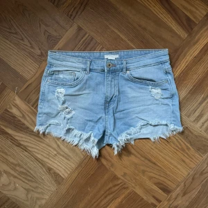 Ljusblå jeansshorts  - Säljer ett par ljusblå jeansshorts med slitna detaljer och fransig kant nertill. Storlek 36. Och ett coolt fransigt hål på backfickan. 