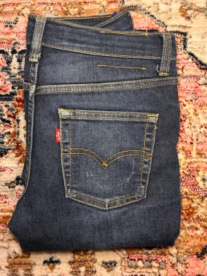 Levis jeans med sköna fades  - Snygga mörkblå jeans från Levi's med klassisk femficksmodell och raka ben. Jeansen har kontrastsömmar i gult och den ikoniska röda Levi's-lappen på bakfickan. Tillverkade i slitstark denim med lätt tvättade detaljer framtill.