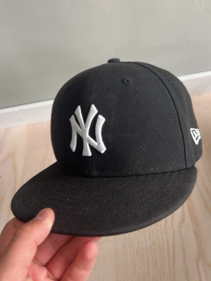 Svart New Era keps - Snygg svart keps från New Era, modell 59FIFTY,  storlek 6 5/8: 53 cm. Den är i väldigt fint skick har bara använts några få gånger. Hör av er om frågor m.m!