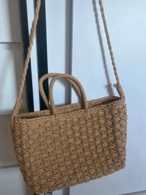 Strandväska  - Snygg beige axelväska/hansväska i flätad strådesign med både handtag och axelrem. Väskan har en rektangulär form och ett trendigt, bohemiskt utseende. Perfekt för dig som gillar naturliga material och vill ha en unik accessoar till din outfit. Köpt i Grekland ☺️ knappt använd 