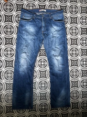 Blå raka jeans från Levi's - Klassiska blå jeans från Levi's med rak passform och fem fickor. Jeansen har en lätt tvättad look med slitningar på låren och knäna. Tillverkade i denim med traditionell knappgylf och bakfickor med Levi's signaturlapp.