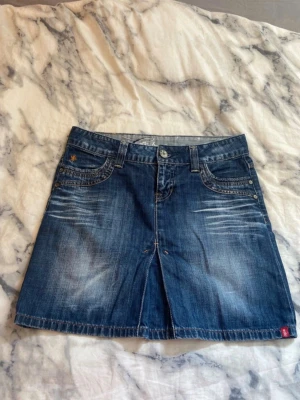 Y2k lågmidjad jeanskjol från esprit  - Snygg blå jeanskjol i kort modell med slitningar framtill och två fickor både fram och bak. Kjolen har klassisk jeanslook med knapp och dragkedja i midjan samt bälteshällor. Perfekt för en avslappnad och trendig stil.