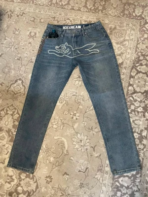 'Billionaire Boys Club' jeans - Säljer ett par blå jeans från Icecream med stort tryck av en tecknad figur på framsidan och broderade glassmotiv på bakfickorna. Jeansen har normal passform och är tillverkade i bomull. Perfekta för dig som vill sticka ut med coola detaljer.