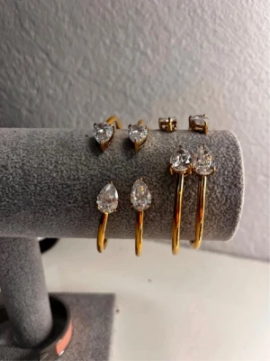 Guldfärgat armband med droppformade stenar - Snyggt armband i guldfärgad metall med två stora, droppformade klara stenar i varje ände. Enkel och stilren design som ger en lyxig känsla. Perfekt för dig som gillar att sticka ut med accessoarerna.