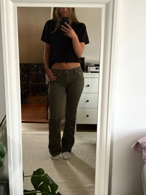 Gröna bootcut jeans - Säljer ett par gröna bootcut jeans med låg midja och klassiska fem fickor. Jeansen har vita sömmar och knappstängning framtill. Snygg passform som framhäver benen och passar perfekt till en avslappnad stil.