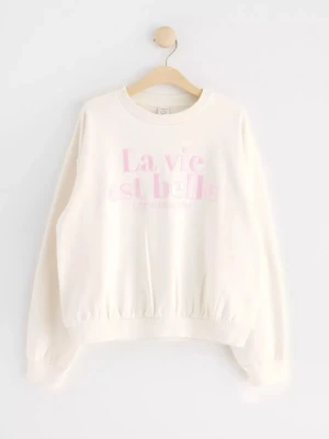 Vit sweatshirt med rosa text La vie est belle. - Säljer en vit sweatshirt med texten 'La vie est belle' i rosa brodyr och 'Life is beautiful' i mindre text under. 