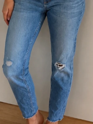 Ljusblå stretch  jeans med slitningar - Säljer ett par ljusblå stretch  jeans med hög midja och raka ben. Jeansen har slitningar på båda knäna för en trendig look. Samt i nedkast av byxbenen .  Byxan  stängs med knapp och dragkedja. Perfekta till vardagsstilen!