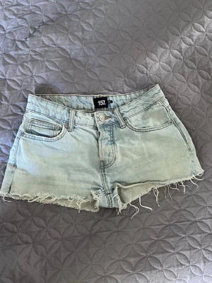 Ljusblå jeansshorts med fransig kant - Säljer ett par ljusblå denimshorts från lager 157 med fransig kant och klassisk femficksmodell. Shortsen har bälteshällor och knappgylf. 