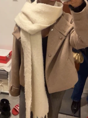 Beige ulljacka med knappar - Snygg beige jacka i ull med bred krage och dekorativa knappar framtill. Jackan har en loose passform och långa ärmar, perfekt för kyligare dagar. Enkel och stilren design som är lätt att matcha.