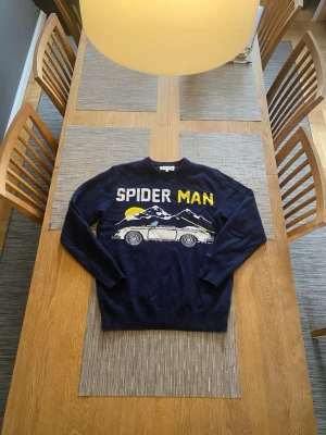 Mörkblå stickad tröja MC2 Saint Barth - Säljer en mörkblå stickad tröja från MC2 Saint Barth med coolt Spider Man-tryck, bergsmotiv och bil på framsidan. Tröjan har rund hals och ribbade muddar. Perfekt för dig som gillar unika och lekfulla plagg. CASHMIR BLEND