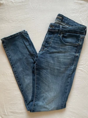 Blå Jack & Jones jeans  - Säljer ett par blå slim fit jeans med klassisk femficksdesign och normalhög midja. Jeansen har en snygg tvättad look och raka ben. Perfekta till sneakers eller boots för en avslappnad stil.
