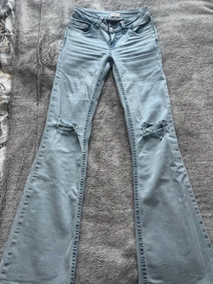 Ljusblå bootcut jeans med slitningar - Säljer ett par ljusblå bootcut jeans med slitna knän och broderade detaljer i rosa på bakfickorna. Superskick och knappt använda. Storlek 32/xxs men är stretchiga och passar mig som brukar ha 34/xs. Från Nelly. Nypris:699kr.  Mitt pris: diskuterbart 