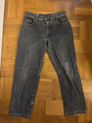 Svarta raka/baggy jeans - Säljer ett par svarta baggy jeans med klassisk femficksmodell och låg midja. Jeansen har en tvättad look och är tillverkade i kraftigt denimtyg. Perfekta för en avslappnad och trendig stil. Ett hål nere på benet, men det går lätt att sy till.
