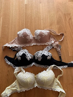 3 spetsbhar i olika färger - Säljer tre bhar från intimissmi med vadderade kupor och vacker spetsdetalj. En beige, en svart och en ljusgul, alla med vit spets upptill och längs kanten. Samtliga har bygel och justerbara axelband för bästa passform. Perfekta för dig som gillar romantisk och feminin stil.