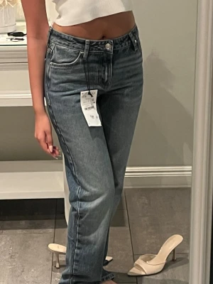 Blå raka jeans med hög midja - Säljer ett par klassiska blå jeans med rak passform och hög midja. Jeansen har fem fickor, bälteshällor och stängs med knapp och dragkedja. Materialet är denim i bomull och de har en snygg tvättad look.