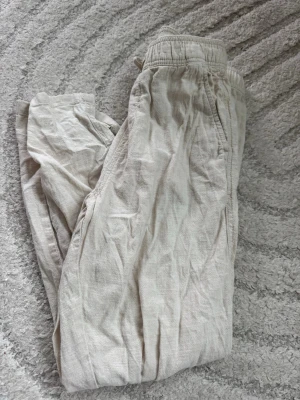 Beiga linnebyxor från H&M - Säljer ett par beiga linnebyxor från H&M med resår och dragsko i midjan. Byxorna har sidfickor och är tillverkade i ett lätt och luftigt linnematerial, perfekta för varma dagar. Passar barn i storlek 134.