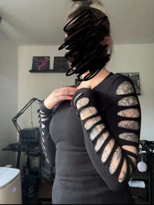 Svart långärmad med hål Alternative - Säljer en svart långärmad topp med cool öppning längs hela ärmarna. Toppen har en tight passform och är perfekt för dig som gillar en edgy stil. Materialet känns mjukt och stretchigt, troligen bomull eller polyester.
