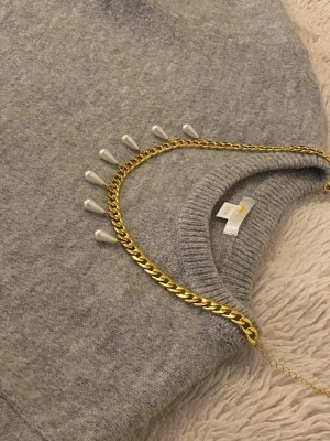 Guldhalsband med droppformade pärlor - Snyggt halsband i guldfärgad rostfritt med kedja och hängande droppformade pärlor. Perfekt för att ge din outfit en trendig touch. Halsbandet har en klassisk kedjedesign och pärlorna ger en elegant kontrast.