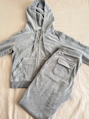 Grått mjukisset juicy couture - Säljer ett grått mjukisset med silvriga detaljer från juciy couture med zip-hoodie och matchande byxor. 